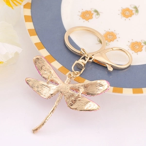 Goldener Libelle Schlüsselanhänger mit rosa Steinen und Karabiner auf floralem Teller