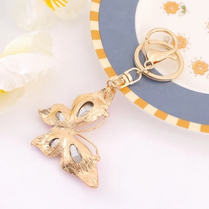 Golden butterfly keychain with sparkling crystals and lobster clasp on decorative ceramic plate