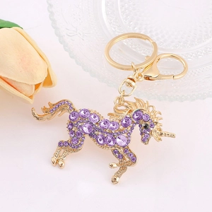 Gros plan du porte-clés licorne dorée avec strass violets sur une surface blanche