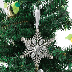 Close-up of a silver metal snowflake ornament with crystals hanging on a green Christmas tree