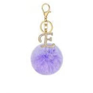 Detail of purple faux fur pompom keychain with golden letter E rhinestone charm