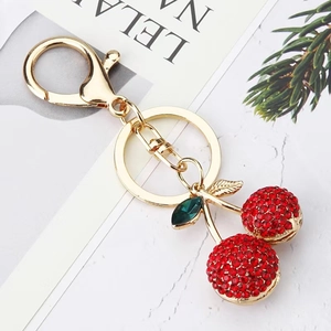 Creative red rhinestone cherry keychain with golden leaves on marble background
