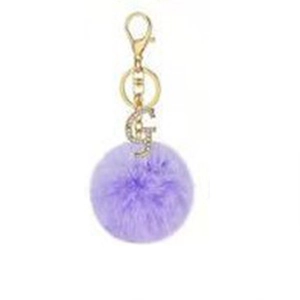 Detail of purple faux fur pompom keychain with golden lobster clasp and rhinestone G pendant