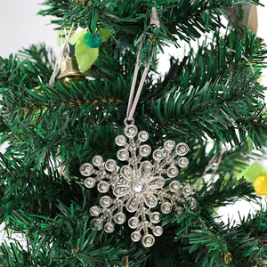 Detail of a sparkling snowflake ornament with rhinestones hanging on a green tree branch