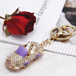 Porte-clés voiture décapotable dorée avec strass et émail violet sur fond de fleurs