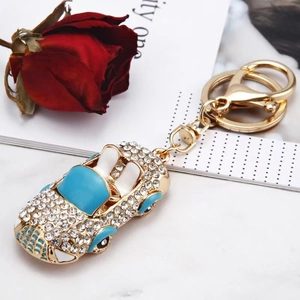 Porte-clés voiture de sport dorée avec strass blancs et détails en émail bleu