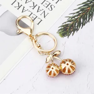 Creative gold-plated cherry keychain with sparkling red rhinestones on a marble surface