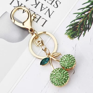 Detail of golden cherry keychain with green rhinestones on marble background