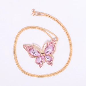 Detail view of a pink crystal butterfly pendant with a golden textured chain necklace