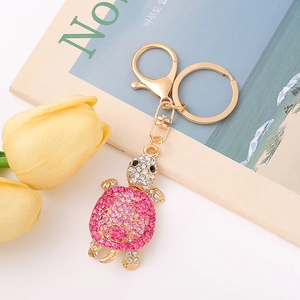 Porte-clés tortue dorée avec cristaux roses et tulipes jaunes sur un magazine