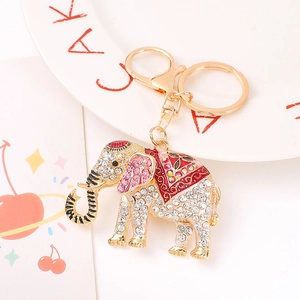 Detail of golden elephant keychain with pink rhinestones and red enamel saddle on white table