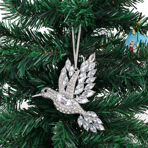 Close-up of silver rhinestone hummingbird ornament hanging with silk ribbon on a tree