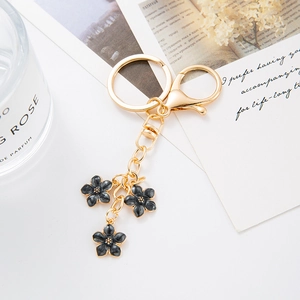 Détail d'un porte-clés doré avec trois fleurs en émail noir sur un fond élégant