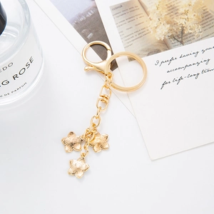 Détail du porte-clés fleur dorée avec trois pendentifs floraux sur un fond blanc épuré