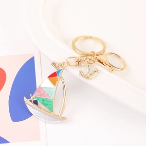 Colorful sailing boat keychain with gold anchor charm on white ceramic background