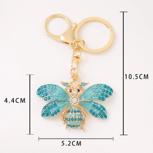 Porte-clés mite dorée avec strass bleu clair sur fond blanc et dimensions de 10,5 cm