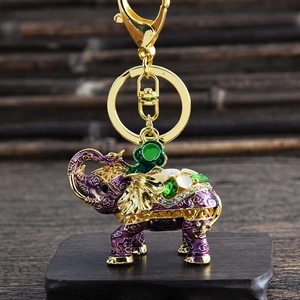 Detail of golden elephant keychain with purple enamel and gemstones on wooden base
