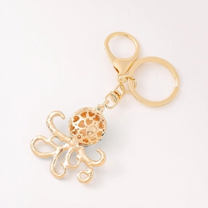 Golden octopus keychain with hollow heart sphere and curved tentacles on white background