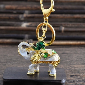 Close-up of white enamel elephant keychain with green gemstones on wooden base