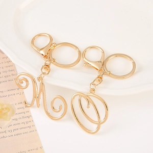 Elegant gold zinc alloy letter M and O keychains with rhinestones on a ceramic tray