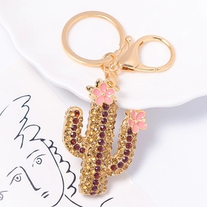 Golden cactus keychain with sparkling rhinestones and pink enamel flowers on a white plate