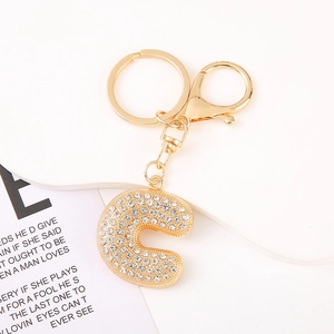 Detail of crystal letter C keychain with golden plating and rhinestones on a white plate