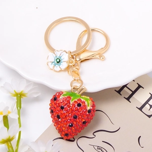Detailed view of red rhinestone strawberry keychain with gold lobster clasp and flower charm