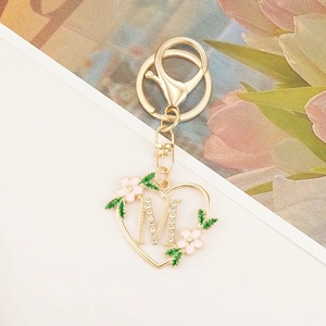 Close-up of golden heart keychain with letter M, pink enamel flower and leaf detail