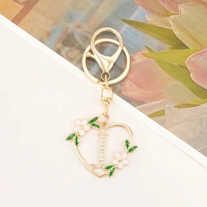 Detail showing heart-shaped golden letter J keychain with rhinestones and floral enamel