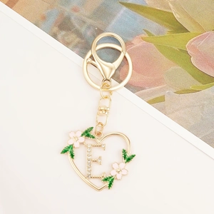 Detail of golden heart-shaped keychain with crystal-studded letter E and floral accents