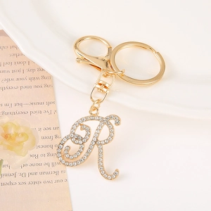 Detail of crystal encrusted golden letter R keychain with lobster clasp on white ceramic