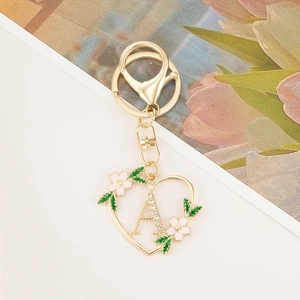Detail of golden heart-shaped keychain with crystal letter A and floral enamel decor