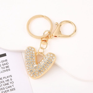 Macro detail of gold-plated heart-shaped letter V keychain encrusted with clear rhinestones