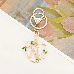 Detailed close-up of golden heart keychain with sparkling crystal letter N and enamel flowers