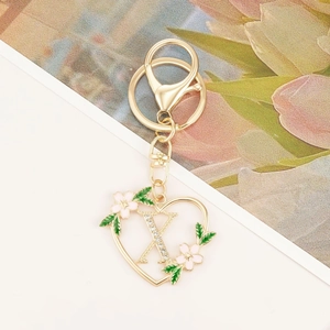 Detailed view of heart-shaped gold keychain with sparkling letter X and floral accents