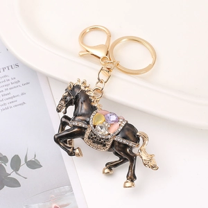 Black enamel horse keychain with colorful crystals and gold plating on a white plate