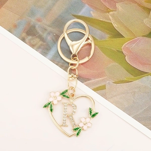 Detail of a heart-shaped gold keychain with rhinestone letter R and enamel floral accents