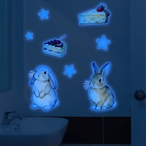 Luminous wall stickers with watercolor rabbits and cakes glowing blue in dark bathroom