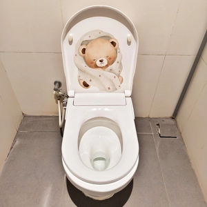 Glow-in-the-dark bear sticker applied to the inner lid of a white bathroom toilet