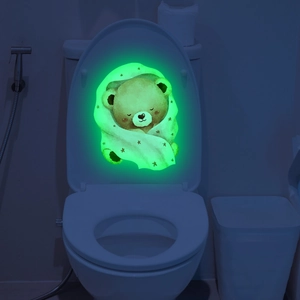 Luminous wall sticker showing a sleeping cartoon bear glowing in green light on toilet lid