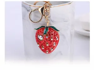 Close-up of strawberry keychain with red rhinestones and golden lobster clasp detail
