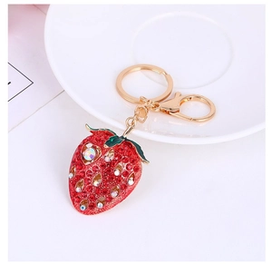 Detail of red rhinestone strawberry keychain with gold plating on a white plate