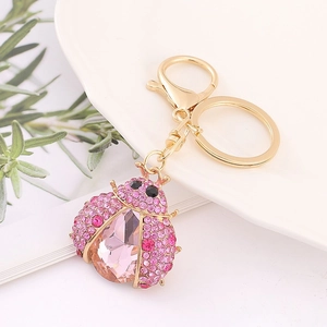 Close-up of a golden ladybug keychain featuring pink rhinestones and crystals on a white plate