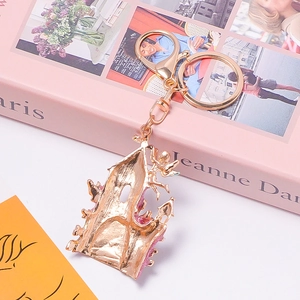 Porte-clés château doré avec petit ange et paillettes roses sur décor élégant