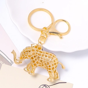 Golden elephant keychain with hollow mesh design and metal swivel clasp on a ceramic dish