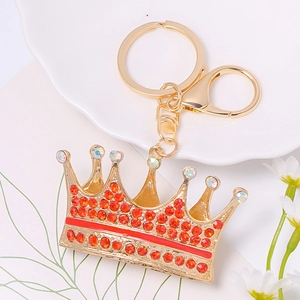 Detail of gold-plated crown keychain with red rhinestones and lobster clasp on white plate