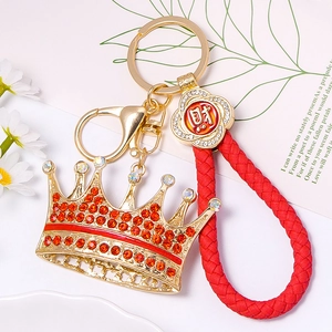 Detail of golden crown keychain with red rhinestones and braided leather rope strap