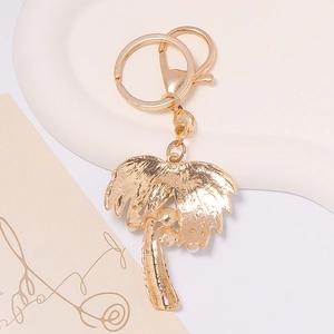 Gold palm tree keychain with pearl accents and metal lobster clasp on a ceramic tray