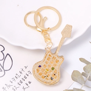 Golden guitar keychain with colorful cat eye stones and sparkling crystals on a white plate