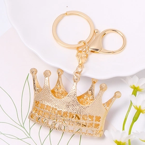 Golden crown keychain with leather rope and rhinestone on white plate with daisy flower